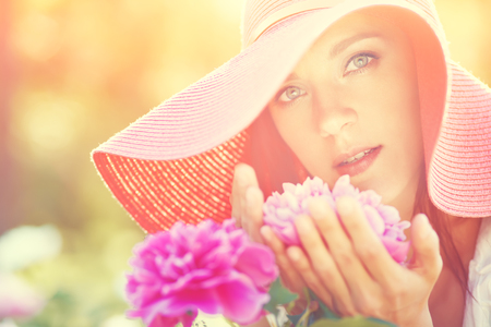 photo with artistic blurring and blur effect. special defocused effect. Vintage toning. film retro style. outdoor closeup portrait of a beautiful middle aged woman. lady in a wide brimmed hat in the park with flowersの写真素材