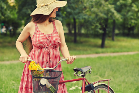young woman in a dress and hat with a bike in a summer park. Active people. Outdoorsの写真素材