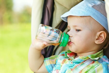 little boy sitting in a stroller and drinks from a bottle. baby for a walk in a pram. summer outdoorsの写真素材