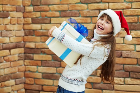 Cute happy teenage girl in santa hat holding a gift. xmas kid