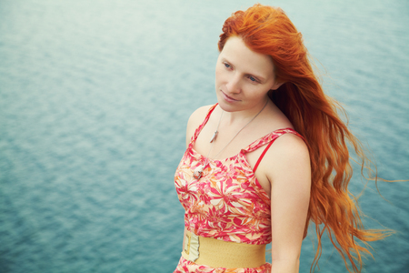 romantic redhead young woman in a dress on sea coastの写真素材