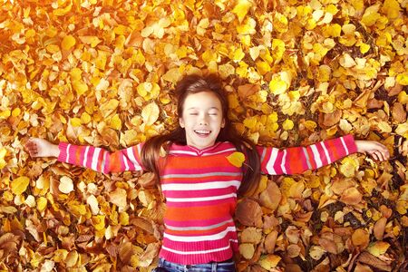 beautiful smiling teenage girl lying on yellow leaves in autumn. top view.の写真素材