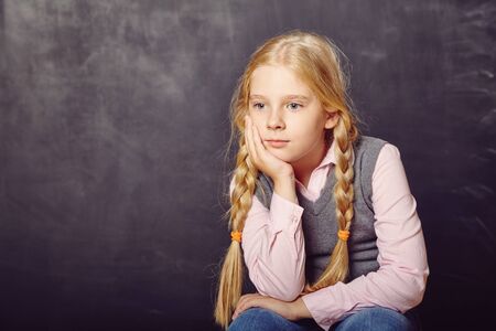 pensive schoolgirl on blackboard background. School and educationの写真素材