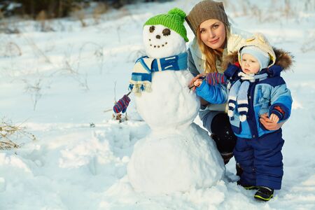 mother and baby in winter park. family outdoors. cheerful mommy with her child with snowmanの写真素材