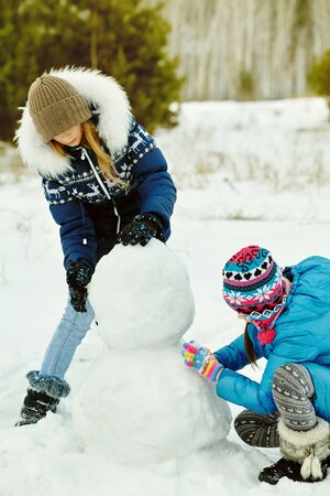 friends building a snowman. funny girls on a walk in the winter outdoorsの写真素材