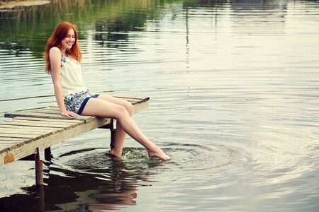 summer portrait of a young redhead woman on background of water in countryside.の写真素材