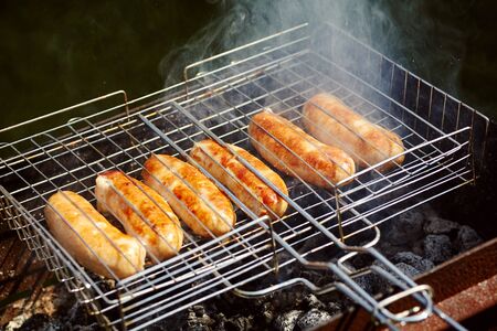 rubicund sausages are roasted on coals. Barbecue on grill in the smokeの写真素材