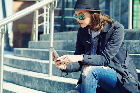 outdoor portrait of a stylish woman in hat and sunglasses with smartphone.の写真素材