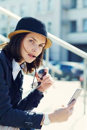 outdoor portrait of a stylish woman in hat and sunglasses with smartphone.の写真素材