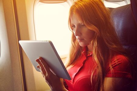 woman in a chair on board aircraft. girl with tablet computer in an airplane. flight and travel.の写真素材