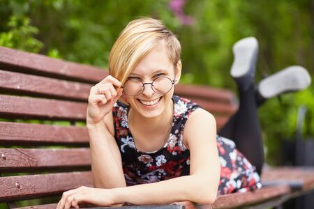 portrait of a beautiful smiling young woman in glasses on a bench in a park.の写真素材