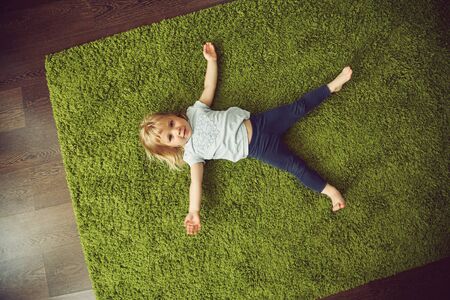 funny little girl lying on a carpet. child playing at home.の写真素材