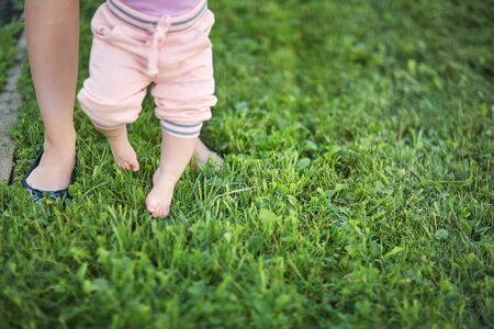 Mother teaching her baby to take the first steps barefoot on the grass.の写真素材