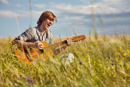 handsome young man with acoustic guitar summer outdoors.の写真素材