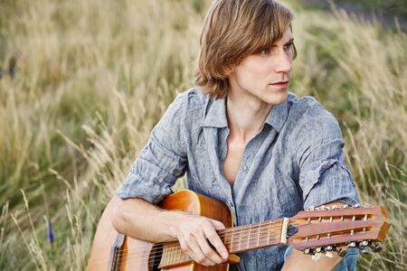 handsome young man with acoustic guitar summer outdoors.の写真素材