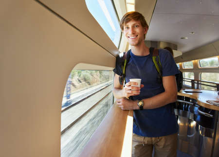 handsome man with a glass of drink riding by train. traveler on the road.の写真素材