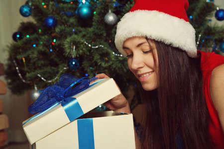woman in santa hat with gift box near Christmas tree.