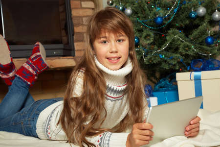 Cute teenage girl with tablet computer near Christmas treeの写真素材