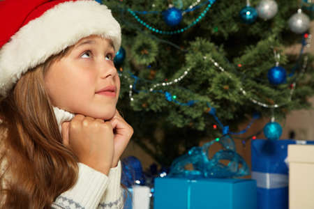 Cute teenage girl in santa hat near Christmas tree.の写真素材