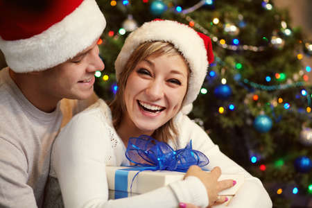 young couple celebrating Christmas at home. man and woman in santa hat with a gift boxの写真素材