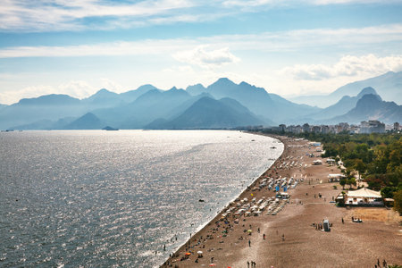 sea beach with people on vacation in sun loungers and sun umbrellas near the water and mountains.の写真素材