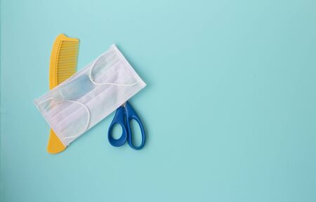 Quarantine haircut. Protective medical mask, disinfectant, comb, scissors on a blue background. Necessary protection against coronavirus.の写真素材