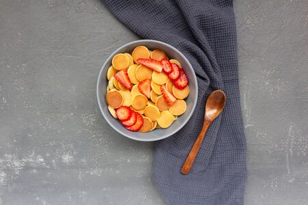 Pancake flakes with sliced strawberries on a gray background with a wooden spoon and a napkin. Tasty trending breakfast.の写真素材