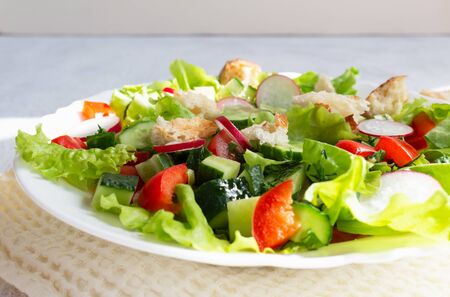 Fattoush salad of vegetables and toasted pita bread in a white plate with a napkin on a light background. Close up. Summer vegetarian saladの写真素材