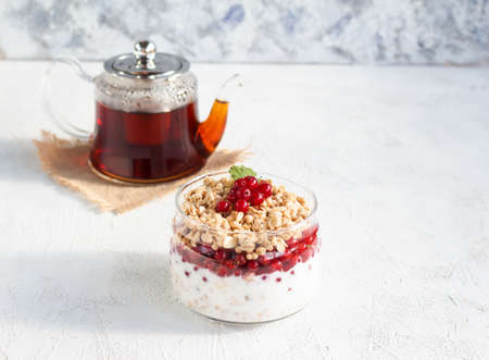 Breakfast with teapot tea and granola in a glass jar with redcurrant berries and yogurt. Place for text on a white backgroundの写真素材