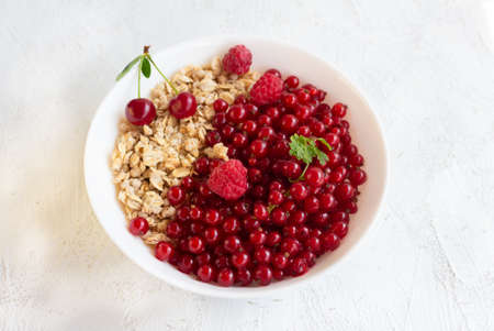 Healthy breakfast of granola and fresh berries of red currant, cherry and raspberry in a white bowl.の写真素材