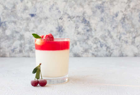 Cold Italian pannacotta dessert in a glass, garnished with frozen raspberries and cherries.の写真素材