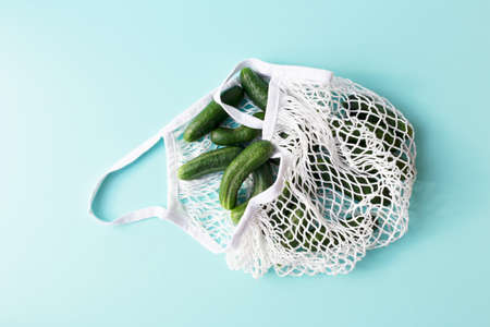 Healthy fresh cucumbers in the white string bag on the blue background. Eco zero waste, no plastic, healthy clean eating concept.の写真素材