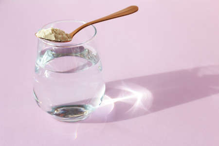 Collagen powder in a spoon and a glass of water on a pink background. Beauty concept. Place for your textの写真素材