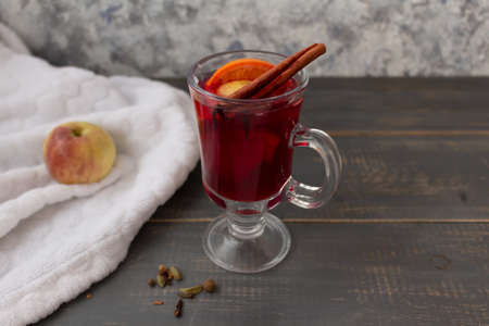 Mulled wine in a glass mug with cinnamon on a wooden table, next to an apple on a blanket.の写真素材
