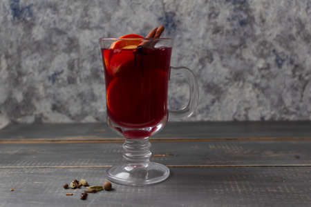 Mulled wine in a glass mug with cinnamon and oranges on a wooden gray tableの写真素材