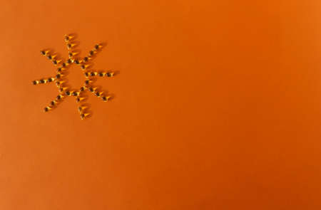 Sun-shaped gelatin capsules on an orange background. Vitamin D. Space for text.の写真素材