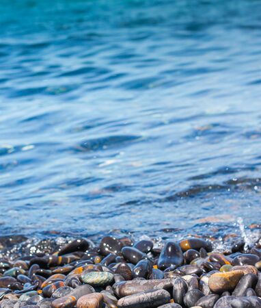 Beautiful black-toned rocks are rounded, curved along the beach, where the seawater is periodically affecting the shore. There is a background sky. In the evening there was a soft light of the sun.の写真素材
