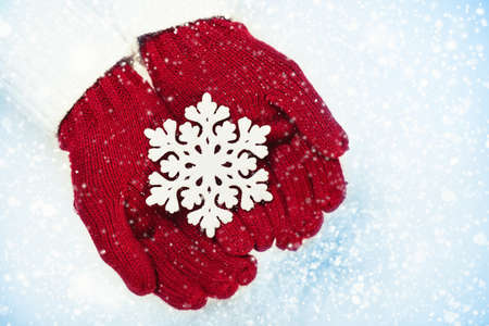 Female hands in mittens with sparkling snowflake on white snow backgroundの写真素材