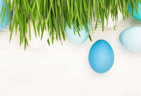 Easter Eggs with green grass on white wooden background