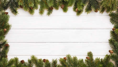 Fir branches with cones on white wooden background