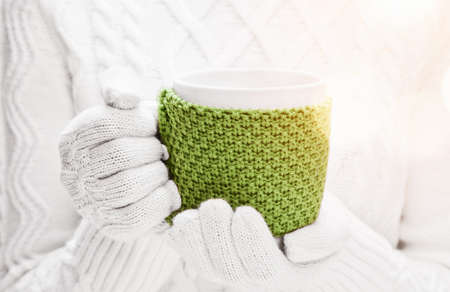 Woman holding winter cup close up in sunshine on light background