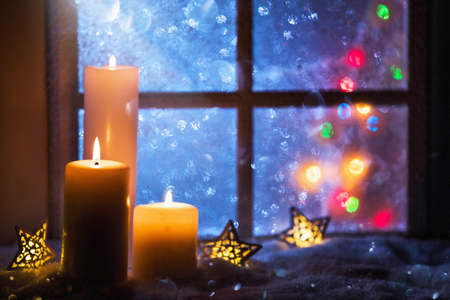 Winter decoration with candles near the snow-covered windowの写真素材