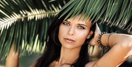 Portrait of beautiful woman hiding behind the palm leavesの写真素材