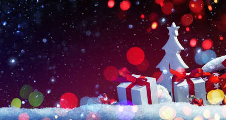 Holidays Decoration with Christmas Tree and Gifts on a Red Background with Colored Lights and Snow Effectsの写真素材