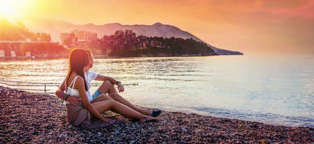 Happy Couple Sits on the Sea Coast at Sunset. Summer Travelsの写真素材