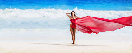 Beautiful Woman with Flying Fabric of Red Color on the Coast of the Oceanの写真素材
