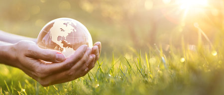 Green planet in female hands against the background of grass and sunbeamsの写真素材