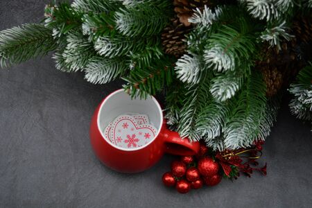 The hears are on the bottom of the cup, The red Christmas decoration lies next to the cup. There is also a part of a Christmas tree decorated with artificial snow and strobiles.の写真素材