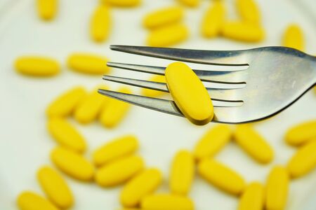 A yellow pill on the fork with dozens of the same pills on the background.  Medical overuse, tablet addictionの写真素材