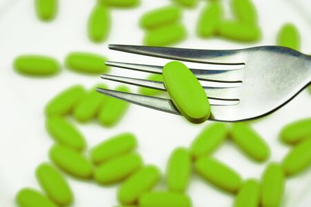 Green pills with fork on white background. Many green pills